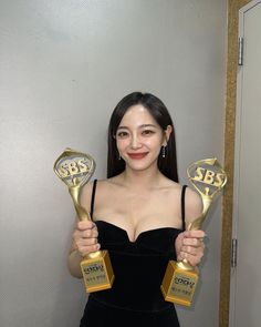 a woman holding two golden awards in her hands and smiling at the camera with one hand up