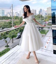 a woman in a white dress is standing on a balcony with her hands behind her back