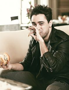 a man sitting on a couch holding a sandwich in one hand and looking at the camera