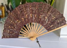 an antique hand fan sitting on top of a white table next to a potted plant