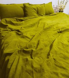 an unmade bed with green linens and white flowers on the nightstand next to it