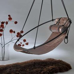 a hammock chair hanging from a metal frame with flowers in a vase on the floor