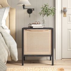 a nightstand with a plant on top of it next to a white door and striped bedding