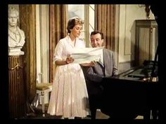 a man and woman standing next to each other in front of a piano with a sheet on it