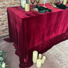 a red table cloth with candles on it in front of a brick wall and flowers