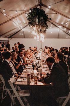 a large group of people sitting at tables in a tent with lights hanging from the ceiling