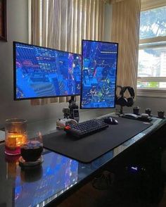 two computer monitors sitting on top of a desk next to a candle and some candles