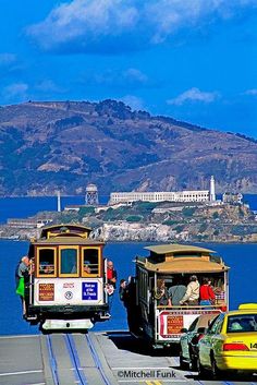 two trolley cars driving down the road next to a yellow car and a yellow taxi