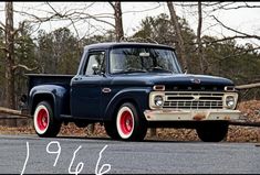 an old pickup truck with red rims parked on the side of the road in front of some trees