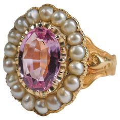 An unapologetically regal natural, untreated pink topaz gemstone is surrounded by a halo of natural uncultured saltwater pearls in this magnificently rare and beautiful unisex ring from the second half of the 19th century. Dating to 1843 and made in London, this 18K yellow gold ring features one of the rarest gemstones in the world: natural pink topaz. Not to be confused with 99% of the pink topaz you may have encountered, which —like blue topaz— owes its color to irradiation. This spectacular pink gem has had no treatment whatsoever. The gem is beautifully cut with tremendous fire. This 12w.5mm x 8.7mm weighs 4 carats and resides within numerous secure hand-carved prongs, surrounded by 18 small, fine natural saltwater pearls. Ornately hand-engraved shoulders lead around to the rear and a Regal Rings, Pearl Gold Ring, Imperial Topaz Ring, Wear Pearls, Saltwater Pearls, Imperial Topaz, Pink Gem, Topaz Necklace, Ring Hand