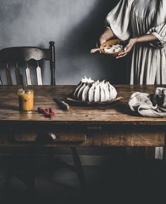 a woman holding a plate with food on it next to a wooden table and chairs