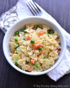 a white bowl filled with pasta and peas on top of a table next to a fork