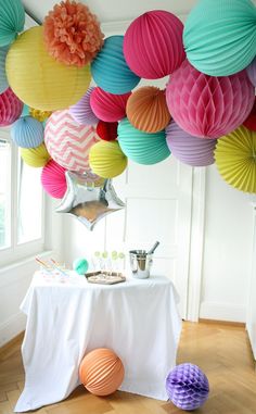 a table topped with lots of colorful paper lanterns next to a white table cloth covered table