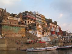 several boats are parked on the shore near some buildings and people walking along the water