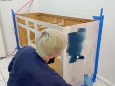 a person painting the walls in a room with blue tape on it and another person holding a paint roller