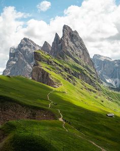 the mountains are covered in green grass and there is a path going through them that leads to a house