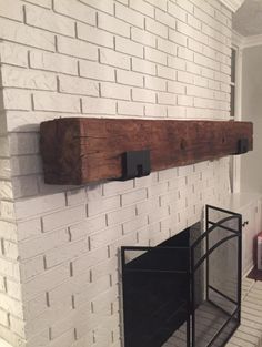 a white brick fireplace with a wooden shelf on the mantle and black metal cage below