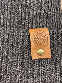 Give the gift of warmth and style! This knit beanie is perfect for hiking, camping, and perfect for keeping warm! Beanie is a dark charcoal gray color, and is made of a soft wool/acrylic blend. Attached is an engraved leather label tag with a brass rivet. The leather label is engraved on both sides, so whether you wear the hat with the brim up or down, the label will still show the design in the correct orientation. Choice of circle logo or trees available at checkout. Care - Hand wash, dry flat Warm Brown Hats For Outdoor Activities, Warm Brown Hat For Outdoor Activities, Windproof Beanie For Fall, Warm Beanie For Outdoor, Outdoor Beanie Cap, One Size Fits Most, Comfortable Beanie For Outdoor Winter Use, Warm Gray Hats For Outdoor, Casual Winter Outdoor Beanie, Comfortable Winter Outdoor Beanie