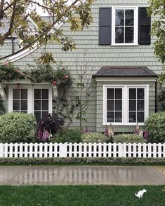 a white picket fence in front of a gray house with windows and flowers on it