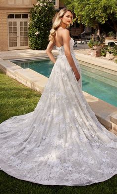 a woman standing in front of a pool wearing a wedding dress with an open back