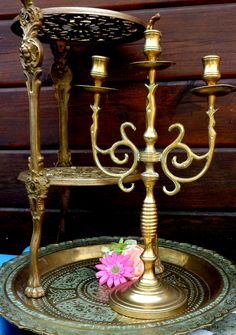 a gold candelabra with three candles and a pink flower sitting on it