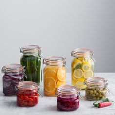 several jars filled with different types of food and vegetables next to each other on a table