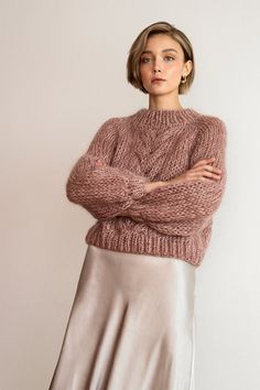 a woman standing with her arms crossed wearing a pink sweater and silver midiskile