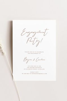 an engagement party card on top of a white surface with a flower in the foreground