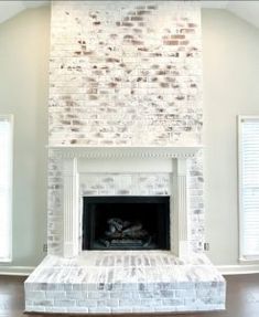 an empty living room with a fireplace and two windows in the corner, all painted white