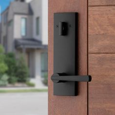 a door handle on the side of a wooden door with a house in the background