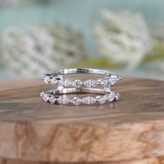 two white gold wedding rings on top of a wooden board with flowers in the background