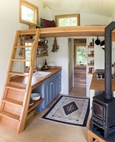 a kitchen area with a stove, sink and ladder to the top floor in a tiny home