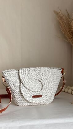 a white handbag sitting on top of a table next to a vase with flowers