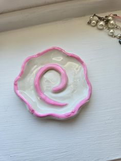 a pink and white ceramic dish sitting on top of a table next to a necklace