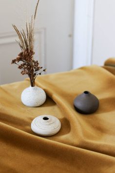 two white vases sitting on top of a brown cloth covered tablecloth with flowers in them