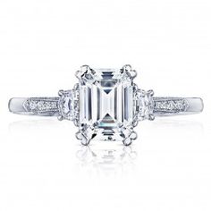 an emerald cut diamond engagement ring with three diamonds on the band and side stones around it