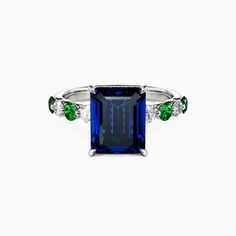 an emerald and blue sapphire ring with three diamonds on the sides, set in white gold