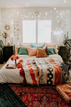 a bed with orange pillows and blankets on it in a room filled with lights, plants and other decorations