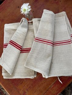 three towels folded on top of a wooden table next to a vase with a flower in it