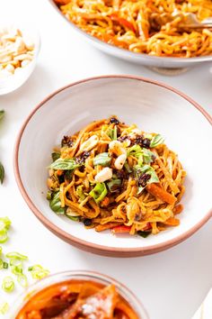 two bowls filled with pasta and vegetables on top of a white tablecloth next to other dishes