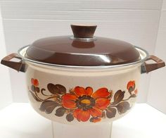 a brown and white casserole with flowers painted on the side sitting on a table