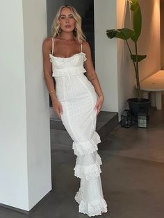 a woman in a white dress leaning against a wall