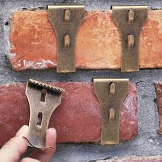 a hand holding an old pair of scissors next to two brick wall hooks on the side of a building