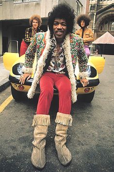 a man sitting on top of a yellow car in front of other people wearing colorful clothing