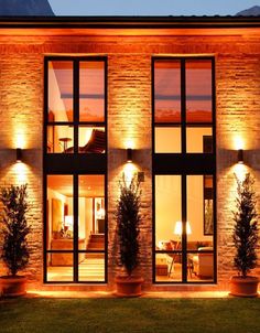 a house that is lit up at night with lights on the windows and potted plants