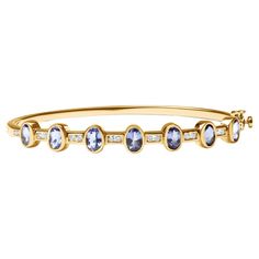 This stunning bangle is a true masterpiece of elegance and beauty. Crafted from 14K yellow gold, this bangle is adorned with 18 sparkling round-cut diamonds, totaling 1/3 carats, with H-I color and I1-I2 clarity. The diamonds are perfectly complemented by 7 radiant oval-cut blue tanzanite gemstones, totaling 3.12 carats. These gemstones have been carefully treated to enhance their natural color, and are set in a bezel setting for a secure and sophisticated look. The bangle is designed to fit wri Gemstone Bangle Bracelets, Bracelet Indian, Diamond Bracelet Design, Gemstone Bangle, Gold Armband, Tanzanite Gemstone, Blue Tanzanite, Box Clasp, Diamond Settings