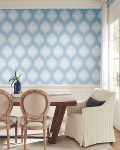 a dining room table with chairs and a vase on top of it in front of a blue wall