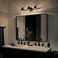 a bathroom vanity with two sinks and a large mirror above it that has lights on