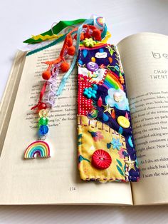 an open book with some colorful beads on it and a rainbow charm hanging from the cover