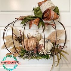 a pumpkin wreath hanging on the front door with fall leaves and acorns around it